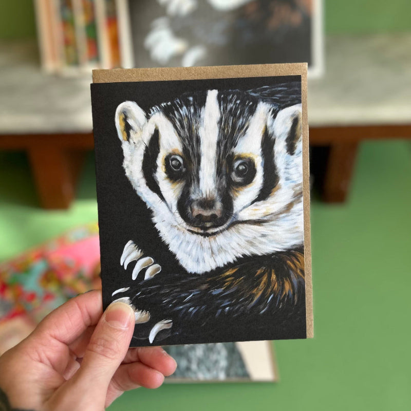 A hand holding a card featuring a high quality print of an oil painting of a badger. 