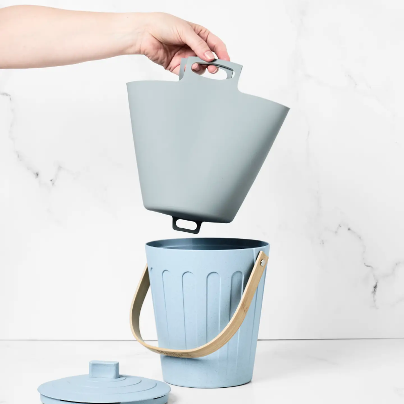 A hand holding the small compost bin liner, lifting it out of the light blue small compost bin.