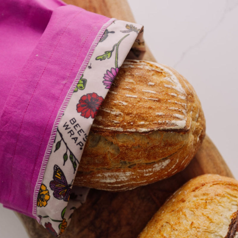 A Magenta Bread bag holding a loaf of bread. Its opening is folded down showing the floral printed bee's wax lining. 
