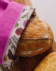 A Magenta Bread bag holding a loaf of bread. Its opening is folded down showing the floral printed bee's wax lining. 
