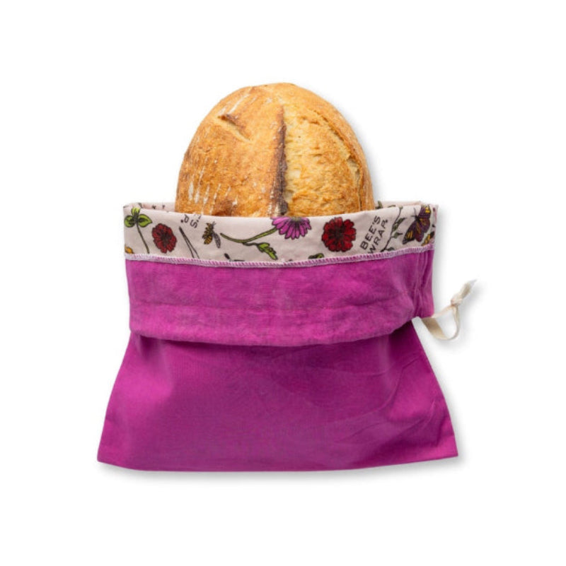 A bright magenta reusable bee's wax lined bread bag with a floral patterned inner lining, shown holding a loaf of bread on a plain white background.