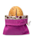 A bright magenta reusable bee's wax lined bread bag with a floral patterned inner lining, shown holding a loaf of bread on a plain white background.