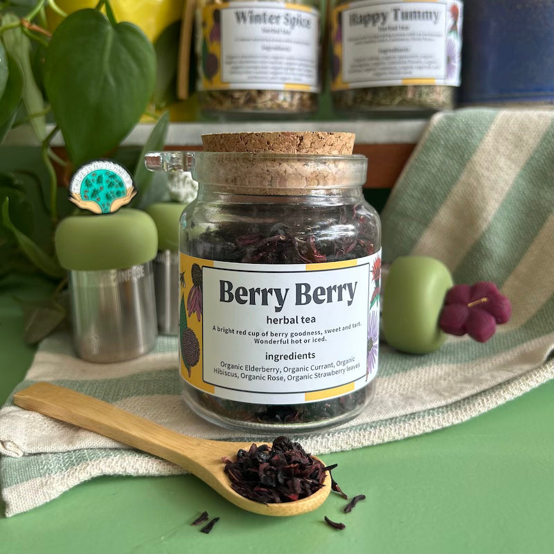 A refillable jar of Berry Berry tea. The jar has a cork lid and an attachable bamboo spoon.