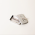 A small, rectangular silver Leaf Razor Blade Safe sits on a plain white background, its lid partly open to reveal several stainless steel blades. One blade engraved I am not plastic rests across the lid. Perfect for safe blade disposal.