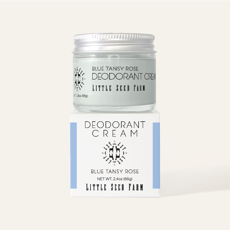 A refillable jar of little seed farm deodorant on top of its blue and white box.
