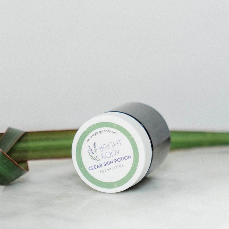 The Bright body Clear Skin Potion  jar on its side showing the lid and the floral logo on it. 