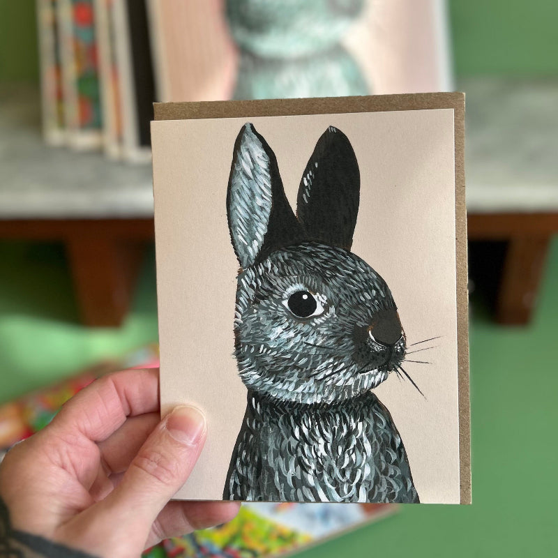 A Hand holding a light pink card featuring a high quality print of an oil painting of a bunny. 