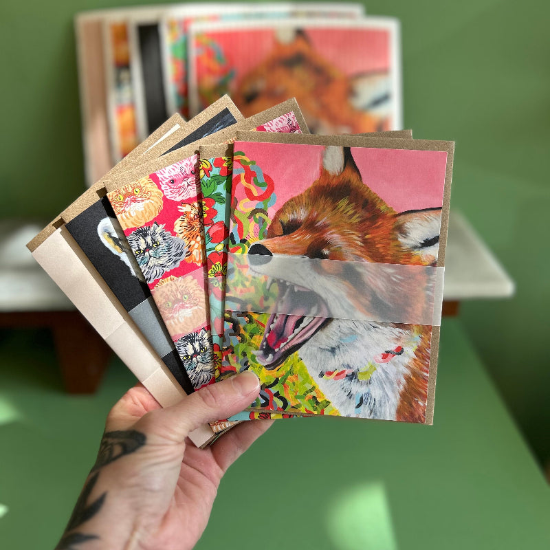A hand hold a fan of greeting cards with high quality prints of oil paintings by  local Madison artist Natalie Jo Wright. 