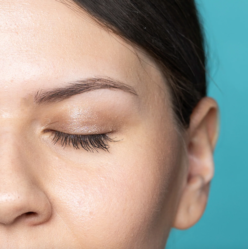 Close-up of a person's face with closed eyes against a teal background. They are wearing the cheekbone mini eyeshadow in the shade brown topaz.