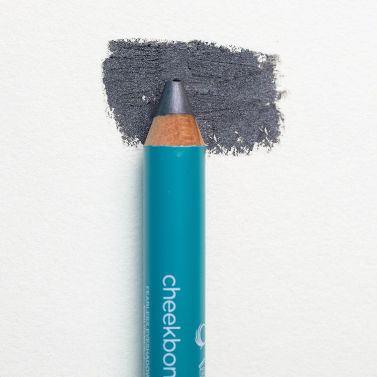 A close up on the Cheekbone Beauty vegan mini eyeshadow pencil and a swatch behind the pencil tip. This is the shade onyx, a smoky charcoal with light shimmer. 