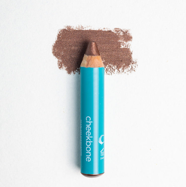 A close up on the Cheekbone Beauty vegan mini eyeshadow pencil and a swatch behind the pencil tip. This is the shade smoky quartz, a rich brown with a light shimmer. 