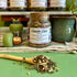 A refillable jar of classic chai tea. The jar has a cork lid and an attachable bamboo spoon. The spoon is in front full of tea.