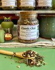 A refillable jar of classic chai tea. The jar has a cork lid and an attachable bamboo spoon. The spoon is in front full of tea.