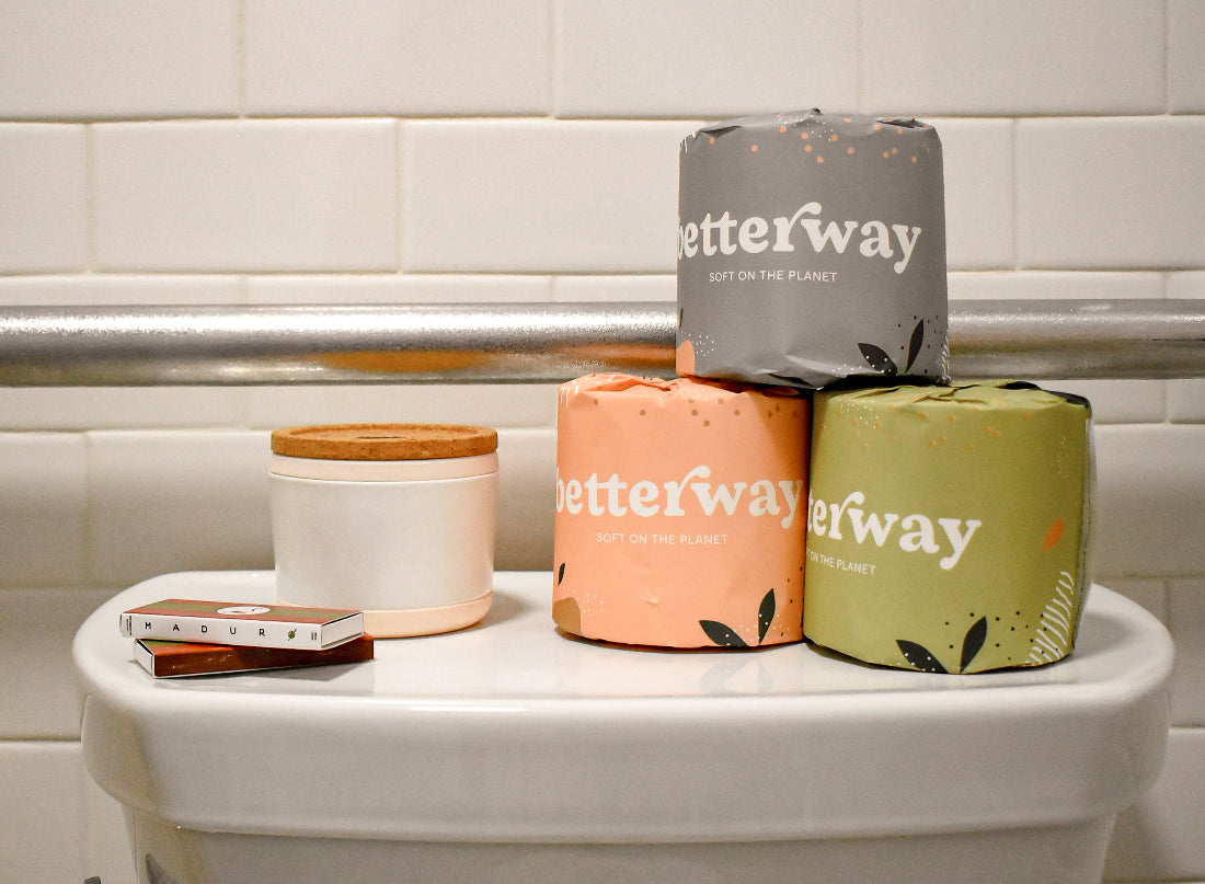 Three rolls of 'betterway' toilet paper on a toilet against a tiled bathroom wall.