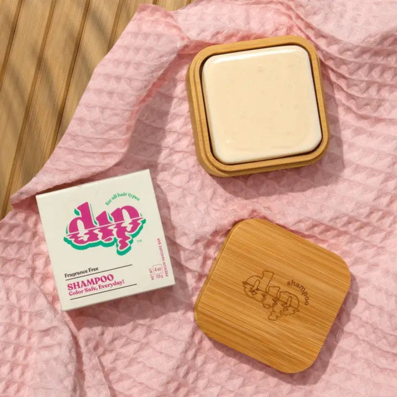 Dip shampoo bar travel case opened up with a shampoo bar inside on a pink fabric background.
