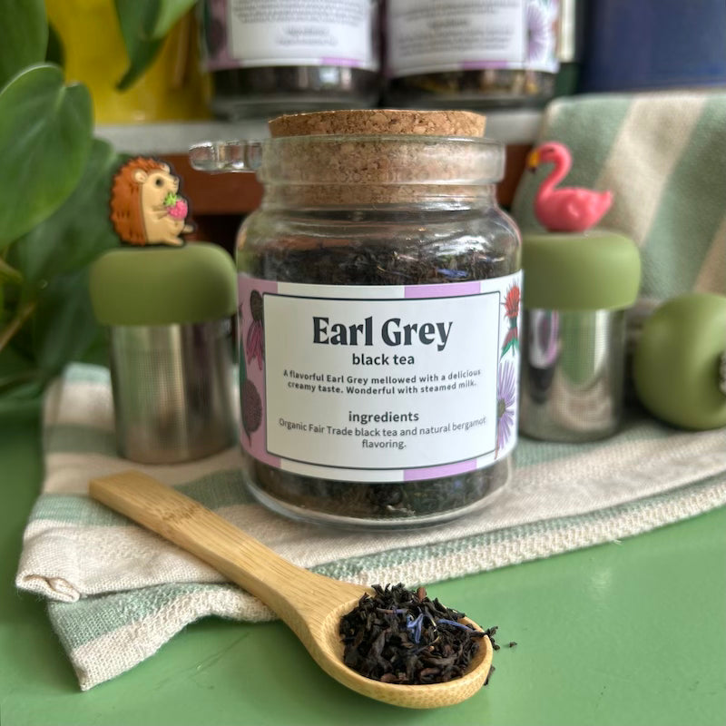 A refillable jar of earl grey tea. The jar has a cork lid and an attachable bamboo spoon.