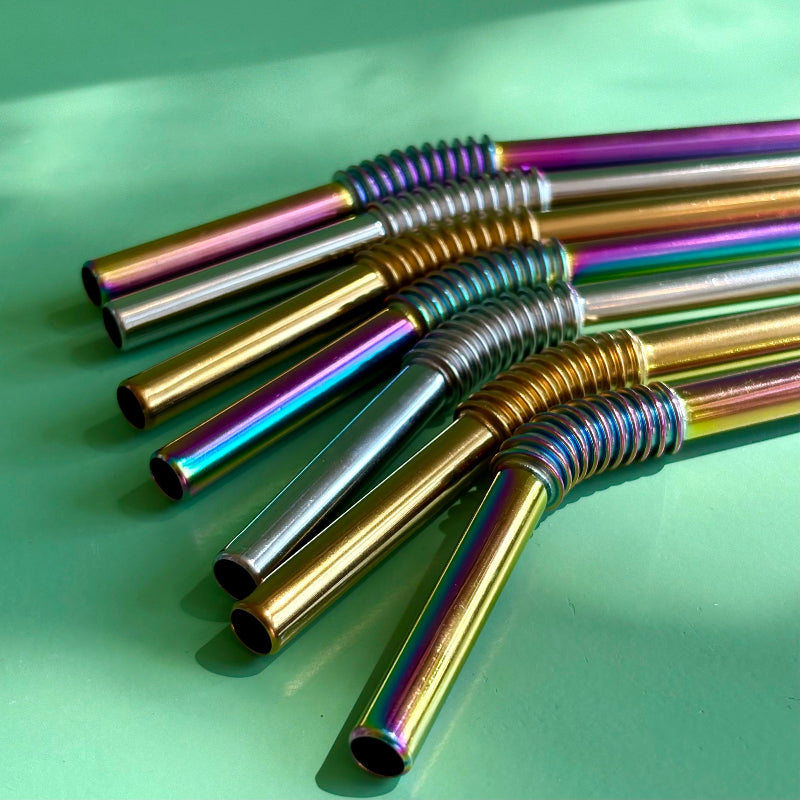 An array of reusable enable metal straws in multiple finishes on a green background. 