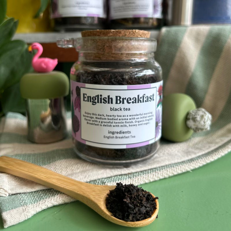 A refillable jar of English breakfast tea. The jar has a cork lid and an attachable bamboo spoon. 