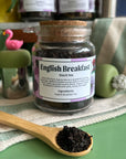 A refillable jar of English breakfast tea. The jar has a cork lid and an attachable bamboo spoon. 