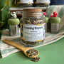 A refillable Jar of Evening repose tea. The jar has a cork lid and an attachable bamboo spoon. The Jar is on a green counter and surrounded by floating tea steepers. 