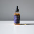 A bottle of Zerra & Co. Face Oil with a dropper cap sits on a white surface in bright sunlight against a plain gray background.