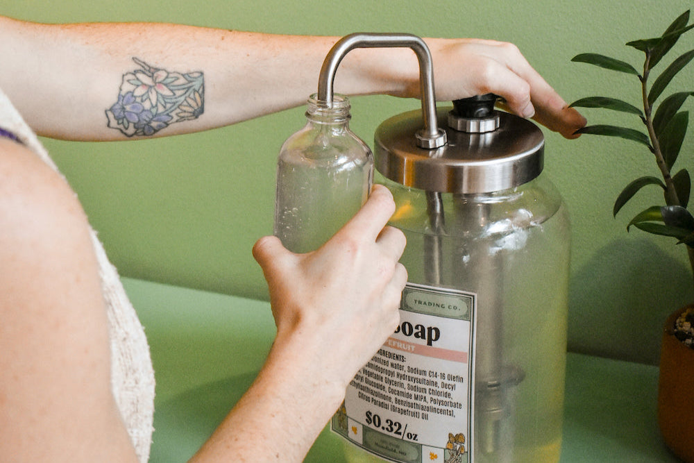 hand pumping dish soap out of bulk container into glass bottle