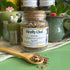 A refillable jar of firefly chai tea. The jar has a cork lid and an attachable bamboo spoon. The spoon is in front of the jar with tea in it. 