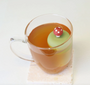 A glass mug from Teany Tiny Kitchen features the Floating Tea Infuser—a green silicone lid with a mushroom-shaped handle—ideal for keeping your tea warm and optimizing steeping.