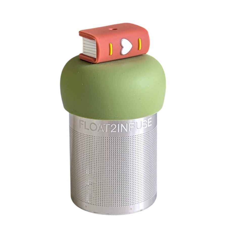 A Stainless steel and silicone floating tea infuser. The top silicone part is green with a brown book with a heart on its spine charm on top of it.