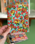 A hand holding a card with a light blue background and bright yellow and red florals. 