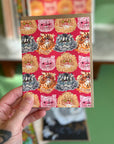 A hand holding a card with a red background and a pattern of several long haired cats.
