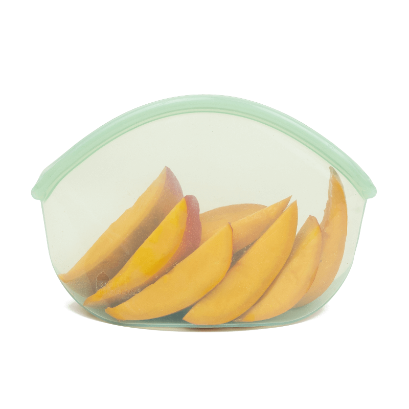 A Green Transparent reusable silicone bag with sliced mango in it on a white background.