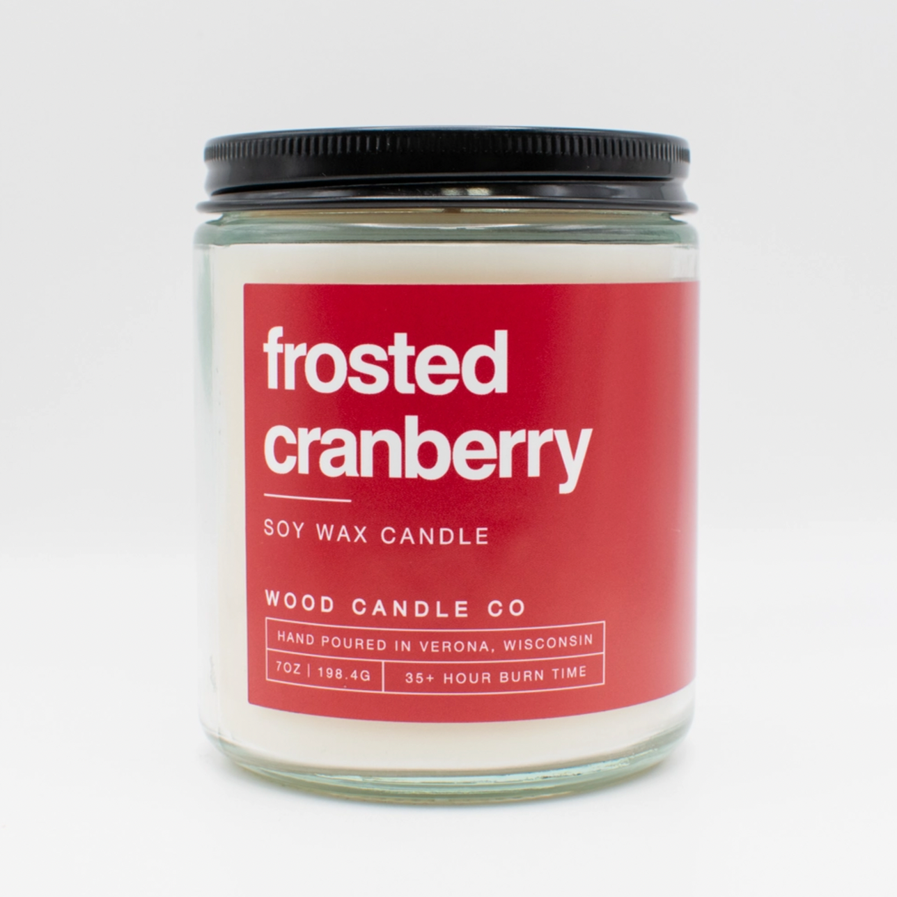 candle jar with red label "frosted cranberry" on white backdrop