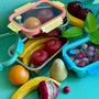 A set of reusable stainless steel containers. Each size has a different colored  glass lid with a steam vent. They are holding wooden fruit on a green background. 