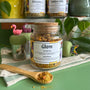 A refillable jar of glow tea. The jar has a cork lid and an attachable bamboo spoon. 