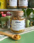 A refillable jar of glow tea. The jar has a cork lid and an attachable bamboo spoon. 