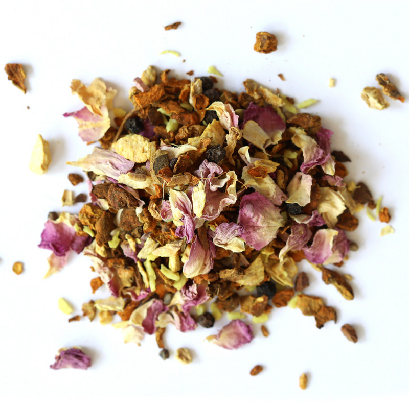 A pile of loose Golden Milk Herbal Tea by Mountain Rose Herbs, a South Indian blend with rose petals, turmeric pieces, masala spices, and herbs scattered on a white background.