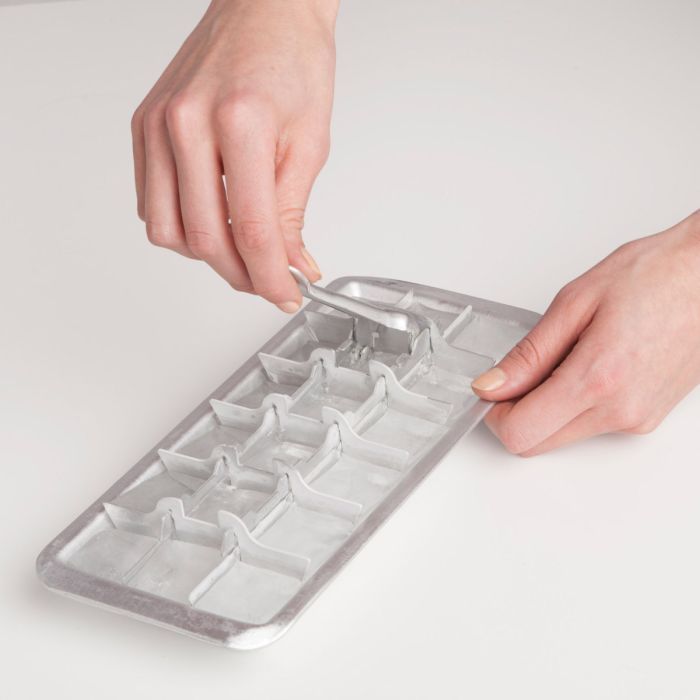 Person using a metal ice cube tray on a light gray background