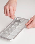 Person using a metal ice cube tray on a light gray background