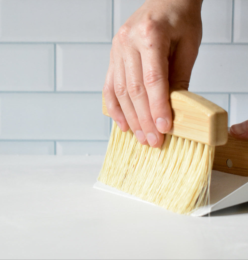 Hand holding a scrub brush against a tiled wall background