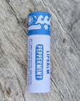A Peppermint Hawaiian Lip balm in a sustainable white paper tube with blue designs on it, sitting on a wooden surface.