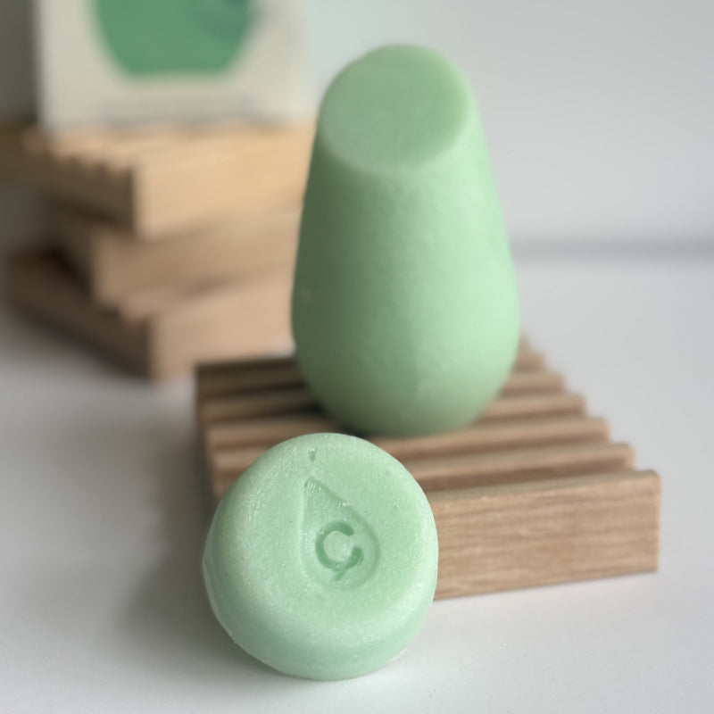 The green hibar mini conditioner in maintain sample leaning on a soap dish in front of the full size conditioner. 