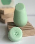 The green hibar mini conditioner in maintain sample leaning on a soap dish in front of the full size conditioner. 