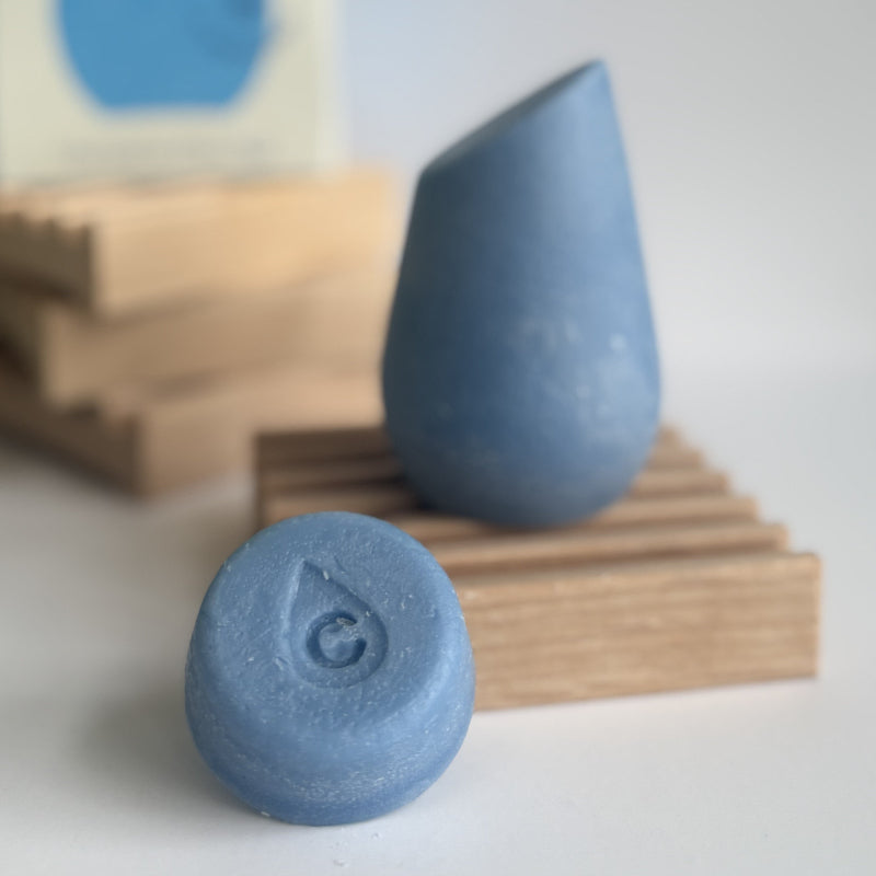 The blue hibar mini conditioner in Moisturizer sample leaning on a soap dish in front of the full size conditioner. 