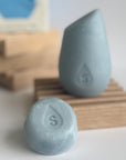 The blue mini hibar moisturize shampoo leaning on a soap dish in front of the full size shampoo bar.