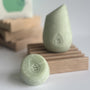 The green mini hibar maintain shampoo leaning on a soap dish in front of the full size shampoo bar.
