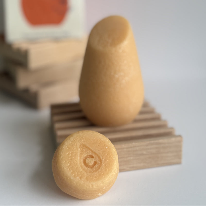 The orange hibar mini conditioner in volumizer sample leaning on a soap dish in front of the full size conditioner. 