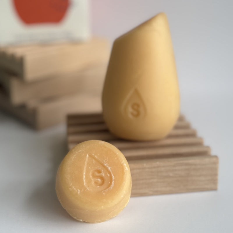 The orange mini hibar volumizer shampoo leaning on a soap dish in front of the full size shampoo bar.