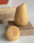 The orange mini hibar volumizer shampoo leaning on a soap dish in front of the full size shampoo bar.
