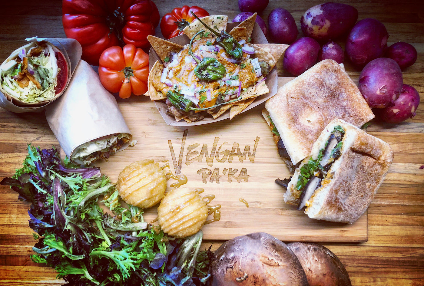 Vegan food platter with wraps, vegetables, and fruits on a wooden board.